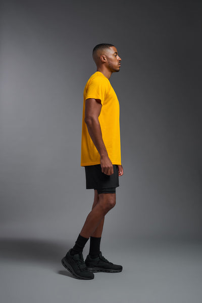 A male african-american model wearing the men's DuroSoft Outdoor Tee in the color yellow on a gray background, made out of 100% filament polyester that feels like soft cotton, showing the modern fit from a side view. This shirt is anti-snagging, quick-drying and moisture-wicking and is made in the USA. #color_yellow