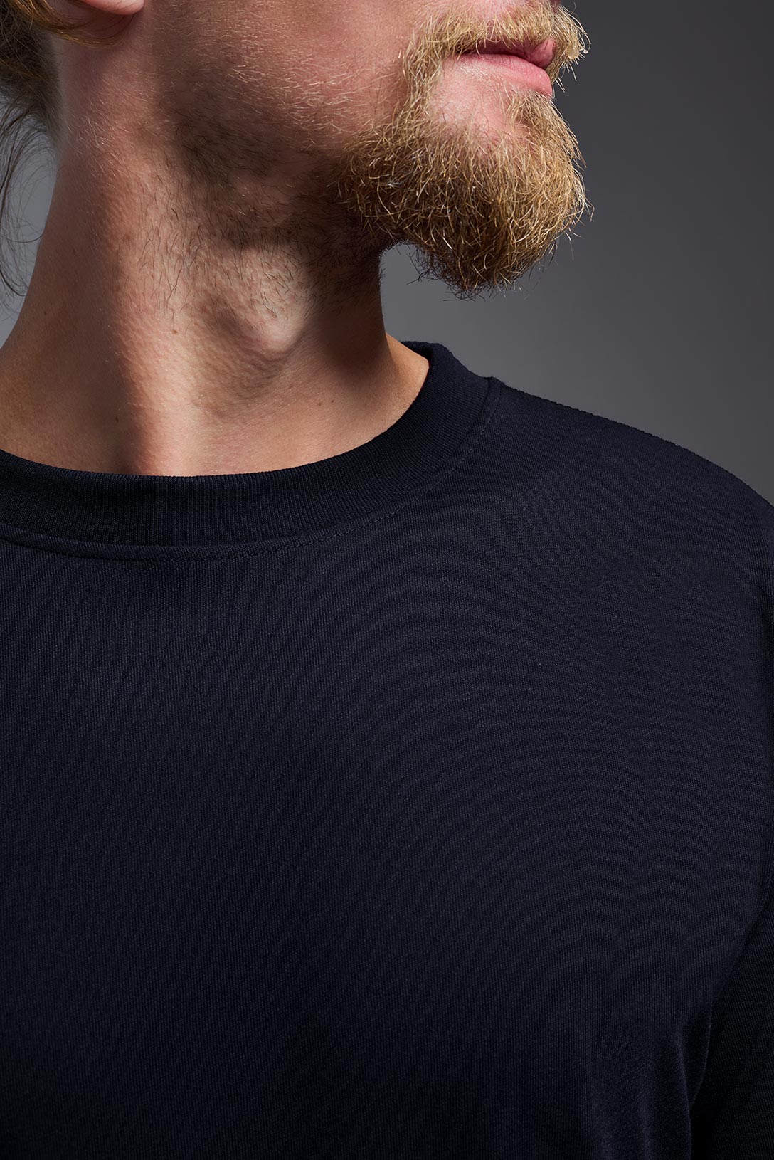 A male Caucasian model with blonde hair and a beard wearing the men's DuroSoft Outdoor Long Sleeve in the color army blue on a gray background, made out of 100% filament polyester that feels like soft cotton, showing the modern fit from a closeup collar view. This shirt is anti-snagging, quick-drying and moisture-wicking and is made in the USA. #color_army-blue