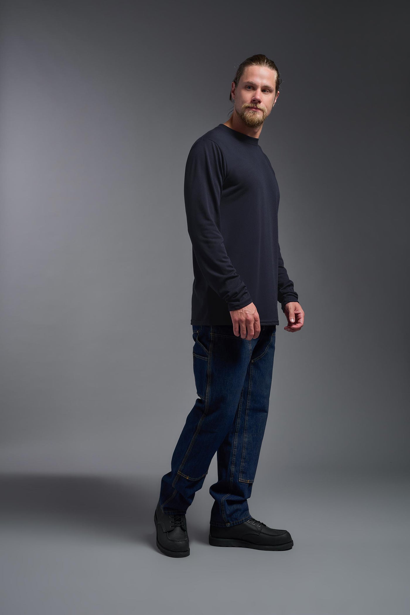 A male Caucasian model with a blonde hair and a beard wearing the men's DuroSoft Outdoor Long Sleeve in the color army blue on a gray background, made out of 100% filament polyester that feels like soft cotton, showing the modern fit from a side view. This shirt is anti-snagging, quick-drying and moisture-wicking and is made in the USA. #color_army-blue