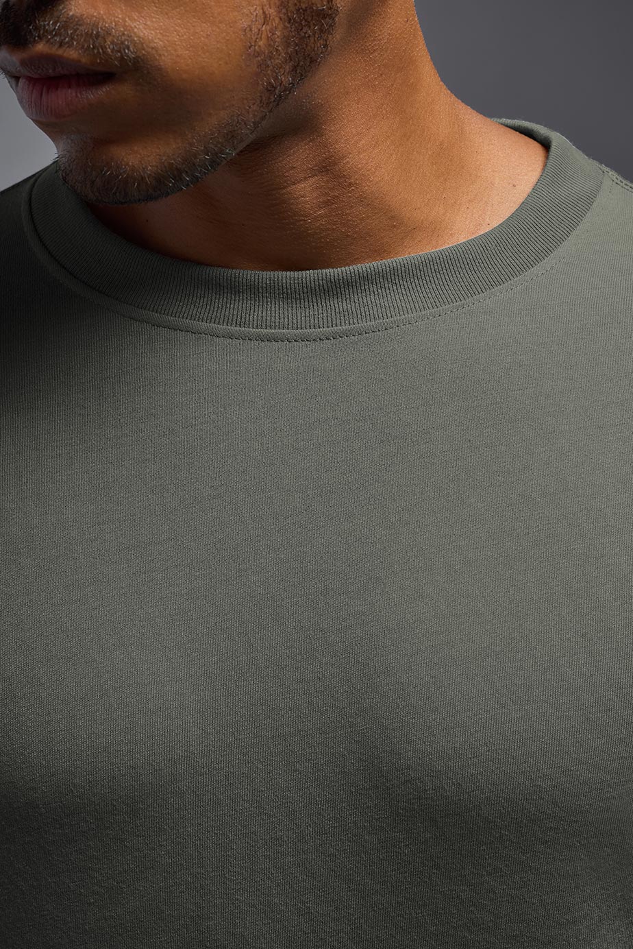 A male Caucasian model with a blonde hair and a beard wearing the men's DuroSoft Outdoor Long Sleeve in the color army gray on a gray background, made out of 100% filament polyester that feels like soft cotton, showing the modern fit from a closeup collar view. This shirt is anti-snagging, quick-drying and moisture-wicking and is made in the USA. #color_army-gray