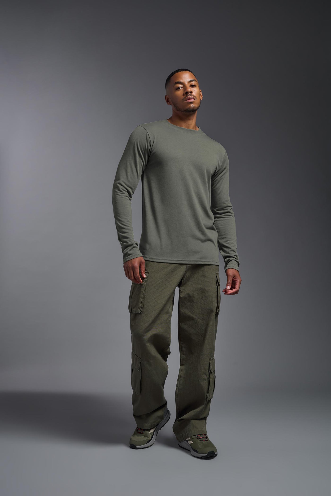 A male Caucasian model with a blonde hair and a beard wearing the men's DuroSoft Outdoor Long Sleeve in the color army gray on a gray background, made out of 100% filament polyester that feels like soft cotton, showing the modern fit from a front view. This shirt is anti-snagging, quick-drying and moisture-wicking and is made in the USA. #color_army-gray