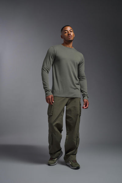 A male Caucasian model with a blonde hair and a beard wearing the men's DuroSoft Outdoor Long Sleeve in the color army gray on a gray background, made out of 100% filament polyester that feels like soft cotton, showing the modern fit from a front view. This shirt is anti-snagging, quick-drying and moisture-wicking and is made in the USA. #color_army-gray