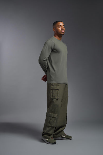 A male Caucasian model with a blonde hair and a beard wearing the men's DuroSoft Outdoor Long Sleeve in the color army gray on a gray background, made out of 100% filament polyester that feels like soft cotton, showing the modern fit from a side view. This shirt is anti-snagging, quick-drying and moisture-wicking and is made in the USA. #color_army-gray