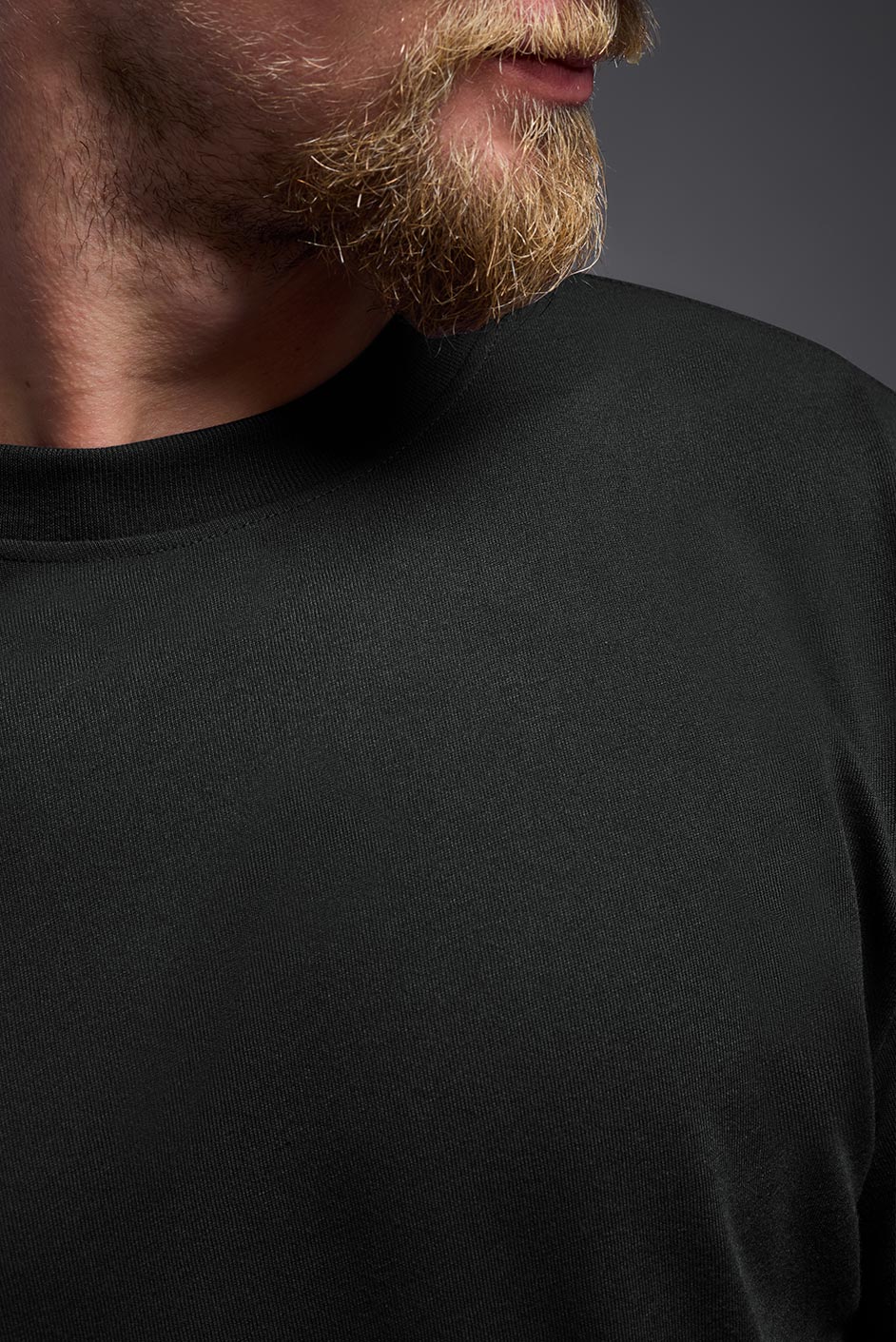 A male Caucasian model with a blonde hair and a beard wearing the men's DuroSoft Outdoor Long Sleeve in the color black on a gray background, made out of 100% filament polyester that feels like soft cotton, showing the modern fit from a closeup collar view. This shirt is anti-snagging, quick-drying and moisture-wicking and is made in the USA. #color_black