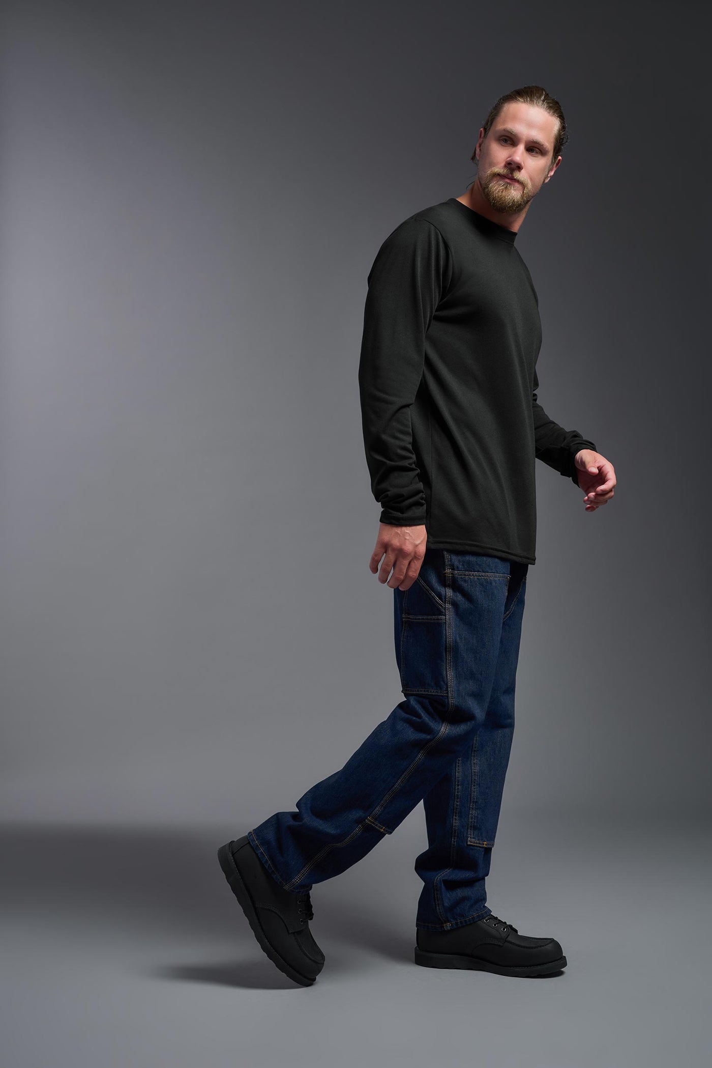 A male Caucasian model with a blonde hair and a beard wearing the men's DuroSoft Outdoor Long Sleeve in the color black on a gray background, made out of 100% filament polyester that feels like soft cotton, showing the modern fit from a side view. This shirt is anti-snagging, quick-drying and moisture-wicking and is made in the USA. #color_black
