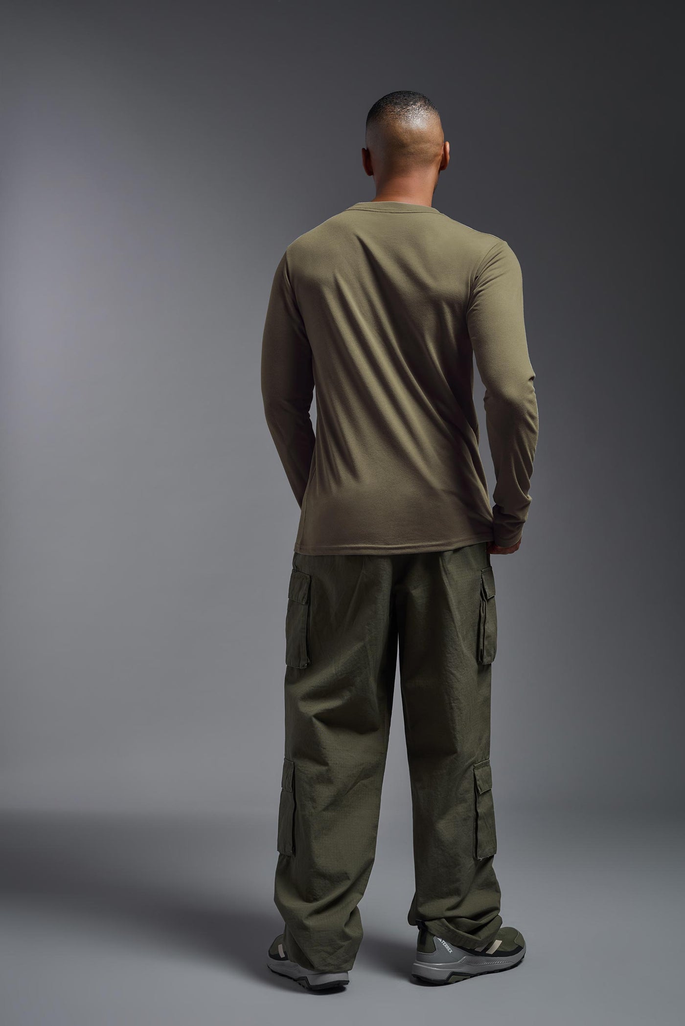 A male African American model with a beard wearing the men's DuroSoft Outdoor Long Sleeve in the color tan 499 on a gray background, made out of 100% filament polyester that feels like soft cotton, showing the modern fit from a back view. This shirt is anti-snagging, quick-drying and moisture-wicking and is made in the USA. #color_tan-499
