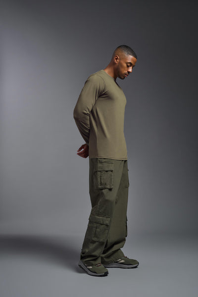 A male African American model with a beard wearing the men's DuroSoft Outdoor Long Sleeve in the color tan 499 on a gray background, made out of 100% filament polyester that feels like soft cotton, showing the modern fit from a side view. This shirt is anti-snagging, quick-drying and moisture-wicking and is made in the USA. #color_tan-499