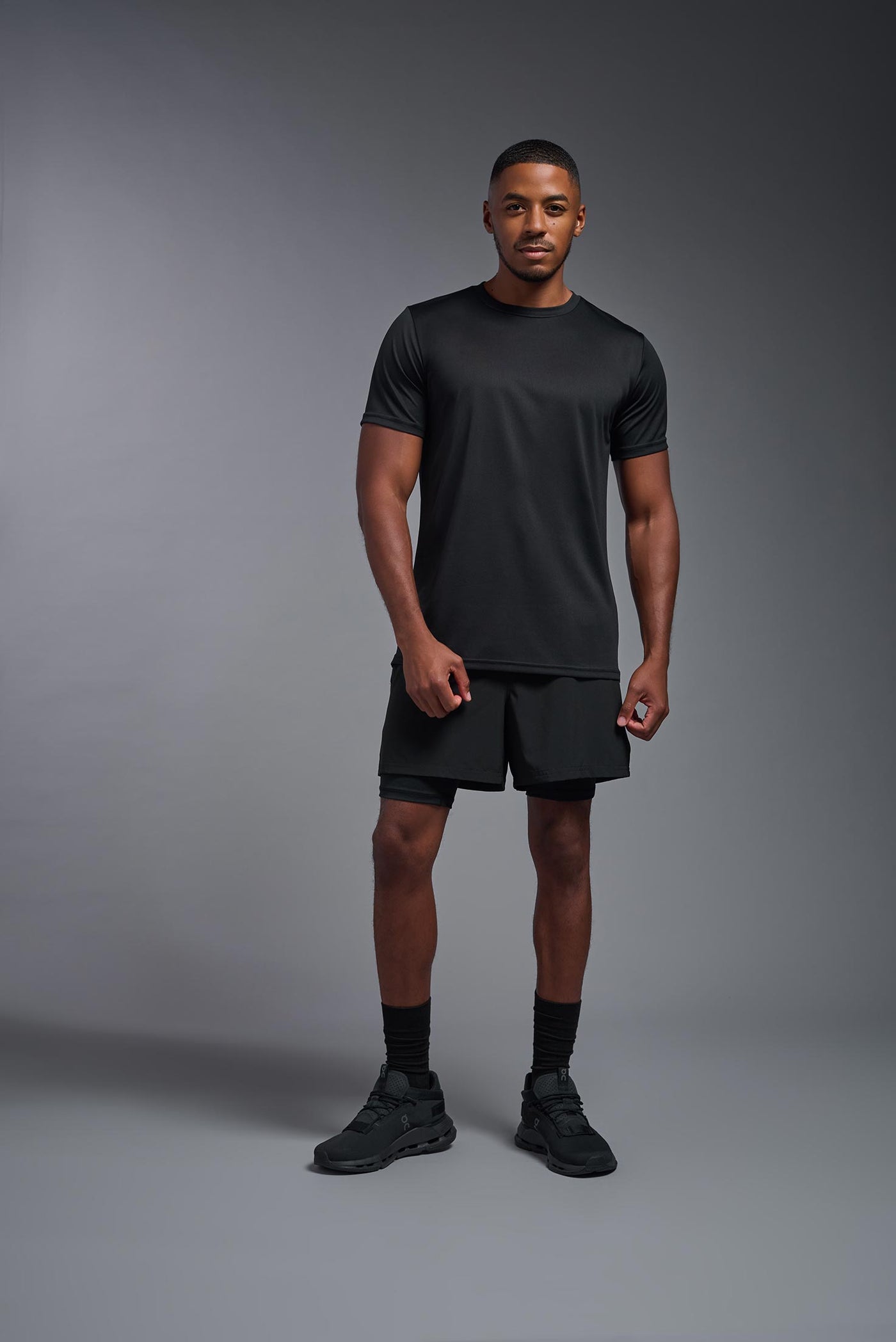 A male African American model witha a beard wearing the men's EcoTek™ Recycled Performance Tee in the color black, made out of 100% recycled polyester REPREVE®, showing the modern fit from a front view. This shirt features a mechanical stretch, quick-dries, wicks moisture and is made in the USA. #color_black