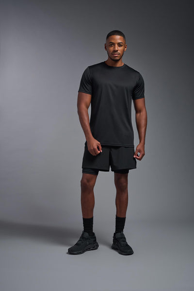 A male African American model witha a beard wearing the men's EcoTek™ Recycled Performance Tee in the color black, made out of 100% recycled polyester REPREVE®, showing the modern fit from a front view. This shirt features a mechanical stretch, quick-dries, wicks moisture and is made in the USA. #color_black