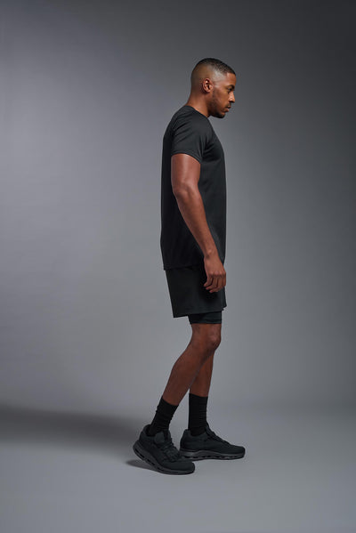 A male blonde model with a beard wearing the men's EcoTek™ Recycled Performance Tee in the color black, made out of 100% recycled polyester REPREVE®, showing the modern fit from a side view. This shirt features a mechanical stretch, quick-dries, wicks moisture and is made in the USA. #color_black