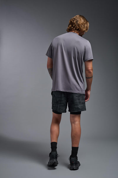 A male blonde model with a beard wearing the men's EcoTek™ Recycled Performance Tee in the color charcoal, made out of 100% recycled polyester REPREVE®, showing the modern fit from a back view. This shirt features a mechanical stretch, quick-dries, wicks moisture and is made in the USA. #color_charcoal