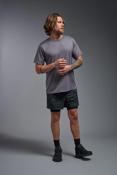 A male blonde model with a beard wearing the men's EcoTek™ Recycled Performance Tee in the color charcoal, made out of 100% recycled polyester REPREVE®, showing the modern fit from a front view. This shirt features a mechanical stretch, quick-dries, wicks moisture and is made in the USA. #color_charcoal