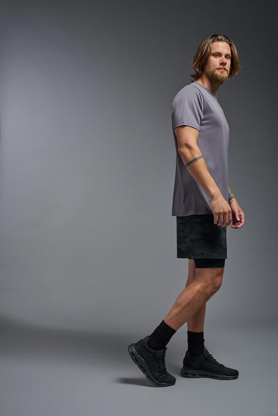 A male, Caucasian, blonde model with a beard wearing the men's EcoTek™ Recycled Performance Tee in the color charcoal, made out of 100% recycled polyester REPREVE®, showing the modern fit from a side view. This shirt features a mechanical stretch, quick-dries, wicks moisture and is made in the USA. #color_charcoal