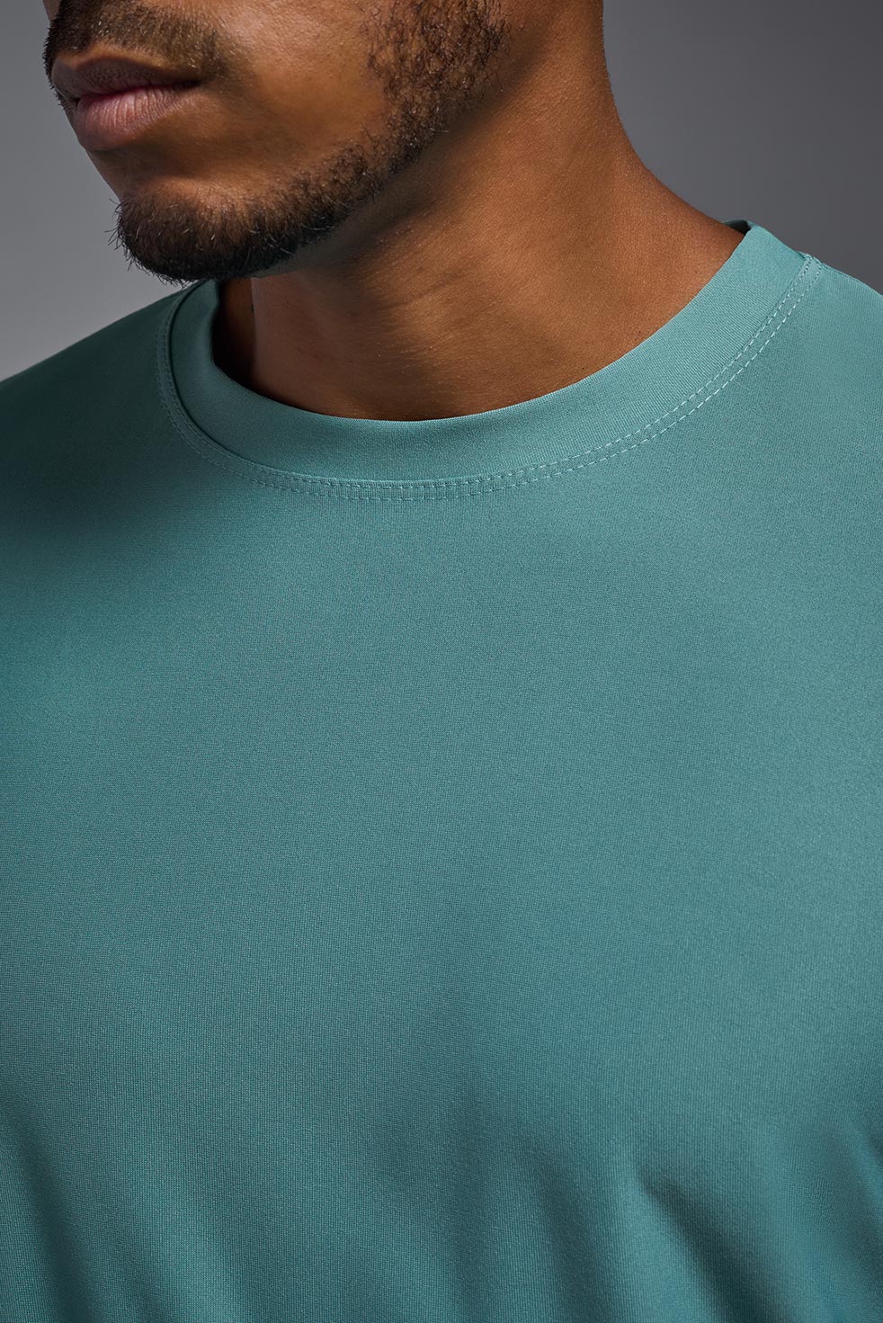 A male African American model with a beard wearing the men's EcoTek™ Recycled Performance Tee in the color juniper, made out of 100% recycled polyester REPREVE®, showing the modern fit from a close-up collar view. This shirt features a mechanical stretch, quick-dries, wicks moisture and is made in the USA. #color_juniper