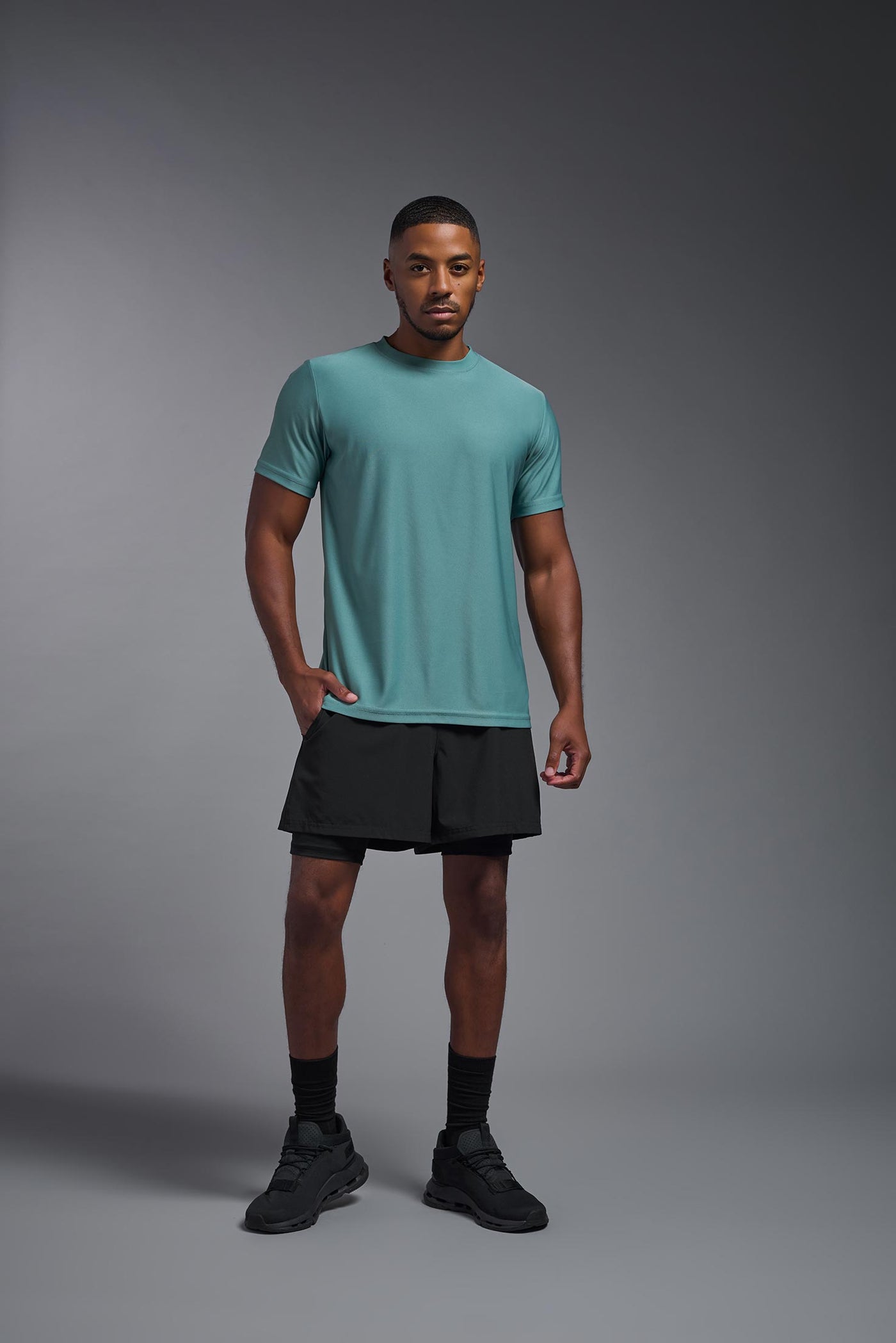 A male African American model with a beard wearing the men's EcoTek™ Recycled Performance Tee in the color juniper, made out of 100% recycled polyester REPREVE®, showing the modern fit from a front view. This shirt features a mechanical stretch, quick-dries, wicks moisture and is made in the USA. #color_juniper