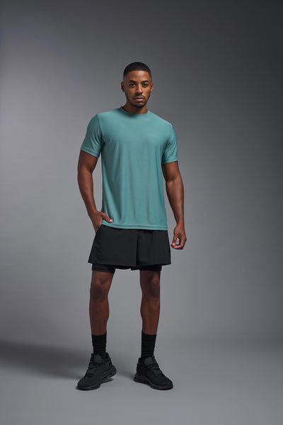 A male African American model with a beard wearing the men's EcoTek™ Recycled Performance Tee in the color juniper, made out of 100% recycled polyester REPREVE®, showing the modern fit from a front view. This shirt features a mechanical stretch, quick-dries, wicks moisture and is made in the USA. #color_juniper