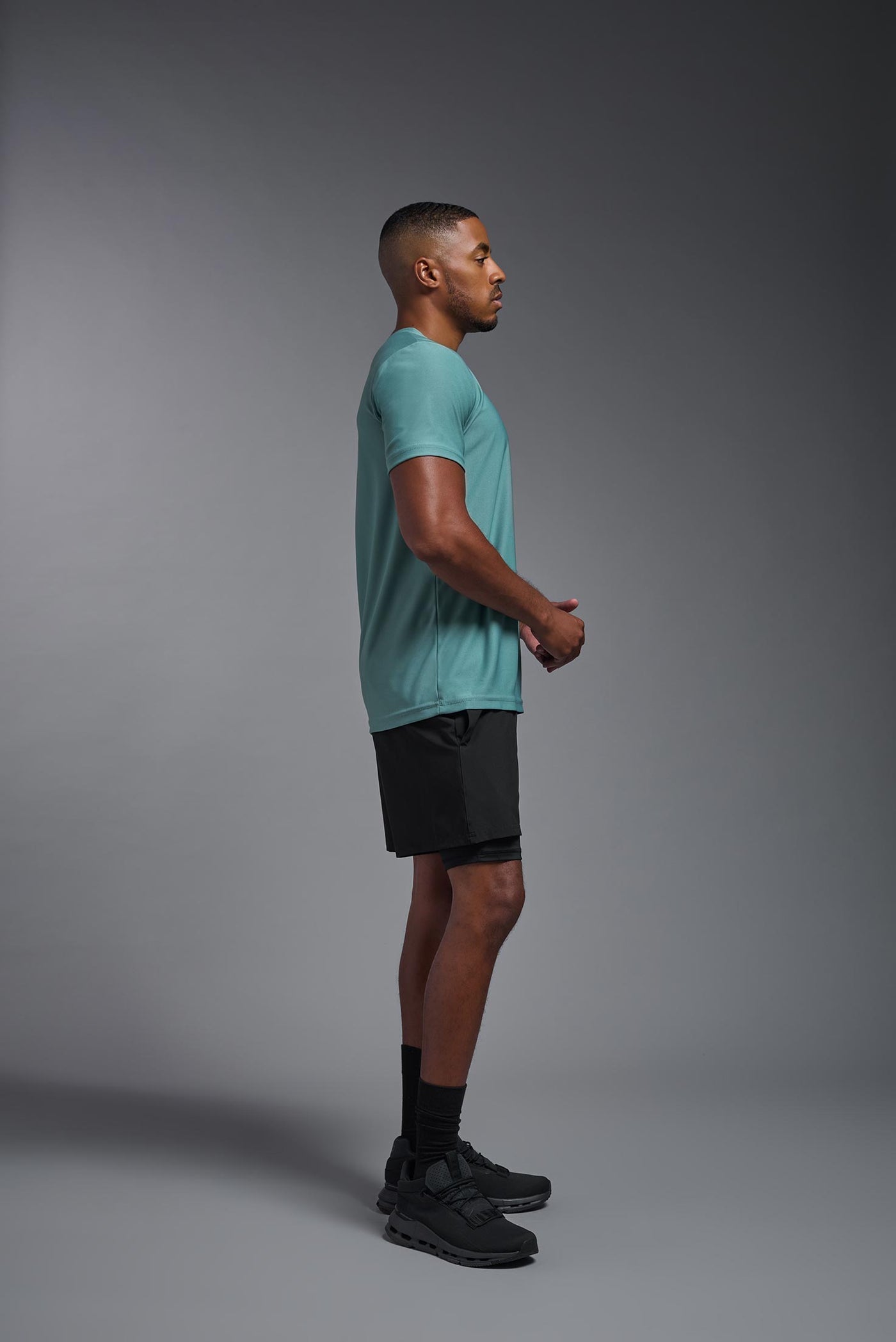 A male African American model with a beard wearing the men's EcoTek™ Recycled Performance Tee in the color juniper, made out of 100% recycled polyester REPREVE®, showing the modern fit from a side view. This shirt features a mechanical stretch, quick-dries, wicks moisture and is made in the USA. #color_juniper