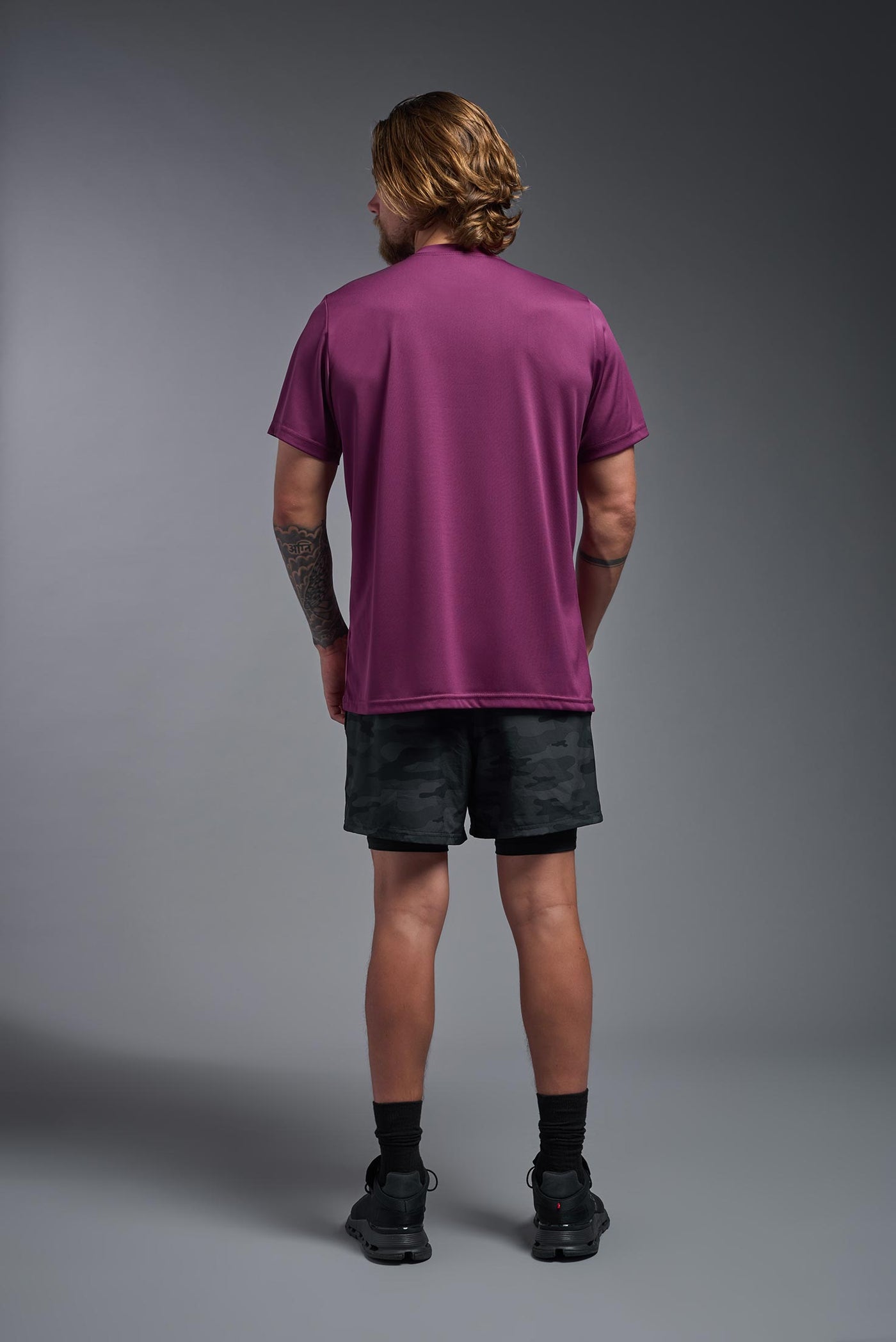 A blonde, male model with a beard wearing the men's EcoTek™ Recycled Performance Tee in the color merlot, made out of 100% recycled polyester REPREVE®, showing the modern fit from a back view. This shirt features a mechanical stretch, quick-dries, wicks moisture and is made in the USA. #color_merlot