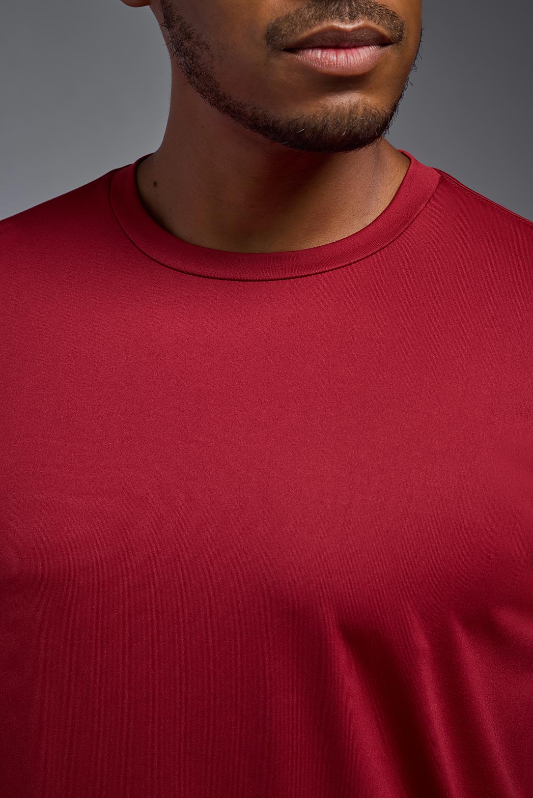 An African American, male model with a beard wearing the men's EcoTek™ Recycled Performance Tee in the color poinsettia, made out of 100% recycled polyester REPREVE®, showing the modern fit from a close-up collar view. This shirt features a mechanical stretch, quick-dries, wicks moisture and is made in the USA. #color_poinsettia