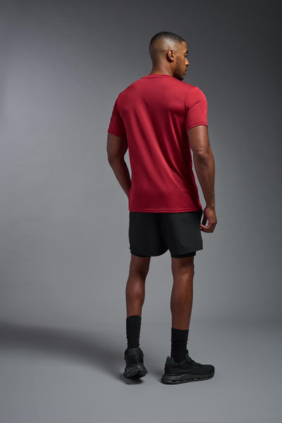 An African American, male model with a beard wearing the men's EcoTek™ Recycled Performance Tee in the color poinsettia, made out of 100% recycled polyester REPREVE®, showing the modern fit from a back view. This shirt features a mechanical stretch, quick-dries, wicks moisture and is made in the USA. #color_poinsettia