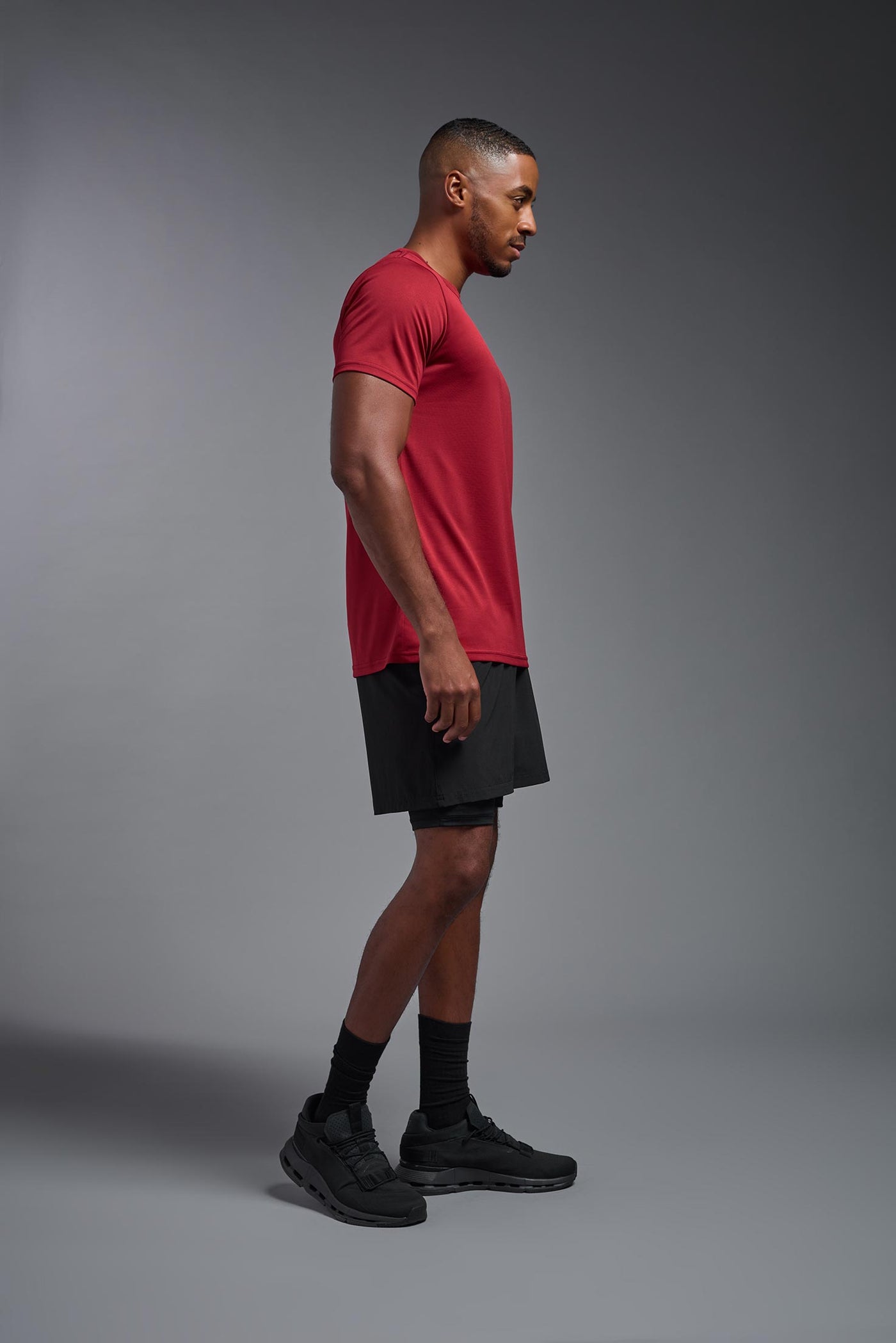 An African American, male model with a beard wearing the men's EcoTek™ Recycled Performance Tee in the color poinsettia, made out of 100% recycled polyester REPREVE®, showing the modern fit from a side view. This shirt features a mechanical stretch, quick-dries, wicks moisture and is made in the USA. #color_poinsettia