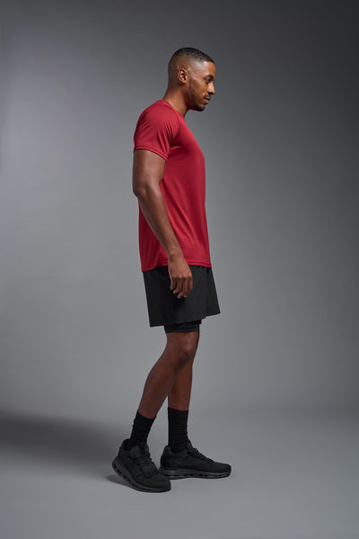 An African American, male model with a beard wearing the men's EcoTek™ Recycled Performance Tee in the color poinsettia, made out of 100% recycled polyester REPREVE®, showing the modern fit from a side view. This shirt features a mechanical stretch, quick-dries, wicks moisture and is made in the USA. #color_poinsettia