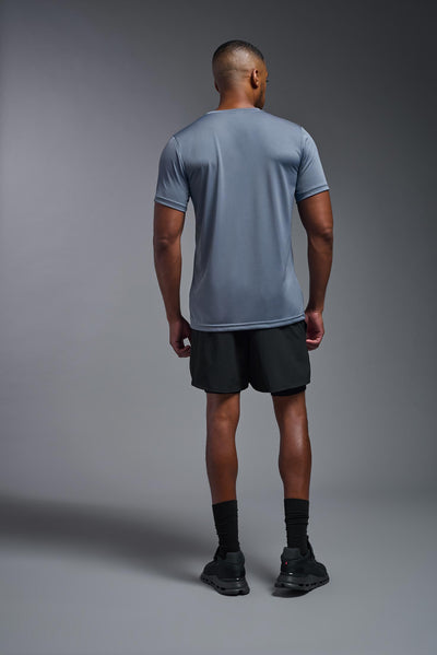 An African American, male model with a beard wearing the men's EcoTek™ Recycled Performance Tee in the color tahoe blue, made out of 100% recycled polyester REPREVE®, showing the modern fit from a back view. This shirt features a mechanical stretch, quick-dries, wicks moisture and is made in the USA. #color_tahoe