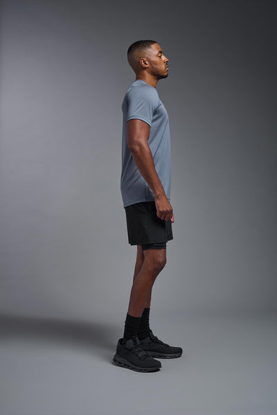 An African American, male model with a beard wearing the men's EcoTek™ Recycled Performance Tee in the color tahoe blue, made out of 100% recycled polyester REPREVE®, showing the modern fit from a side view. This shirt features a mechanical stretch, quick-dries, wicks moisture and is made in the USA. #color_tahoe