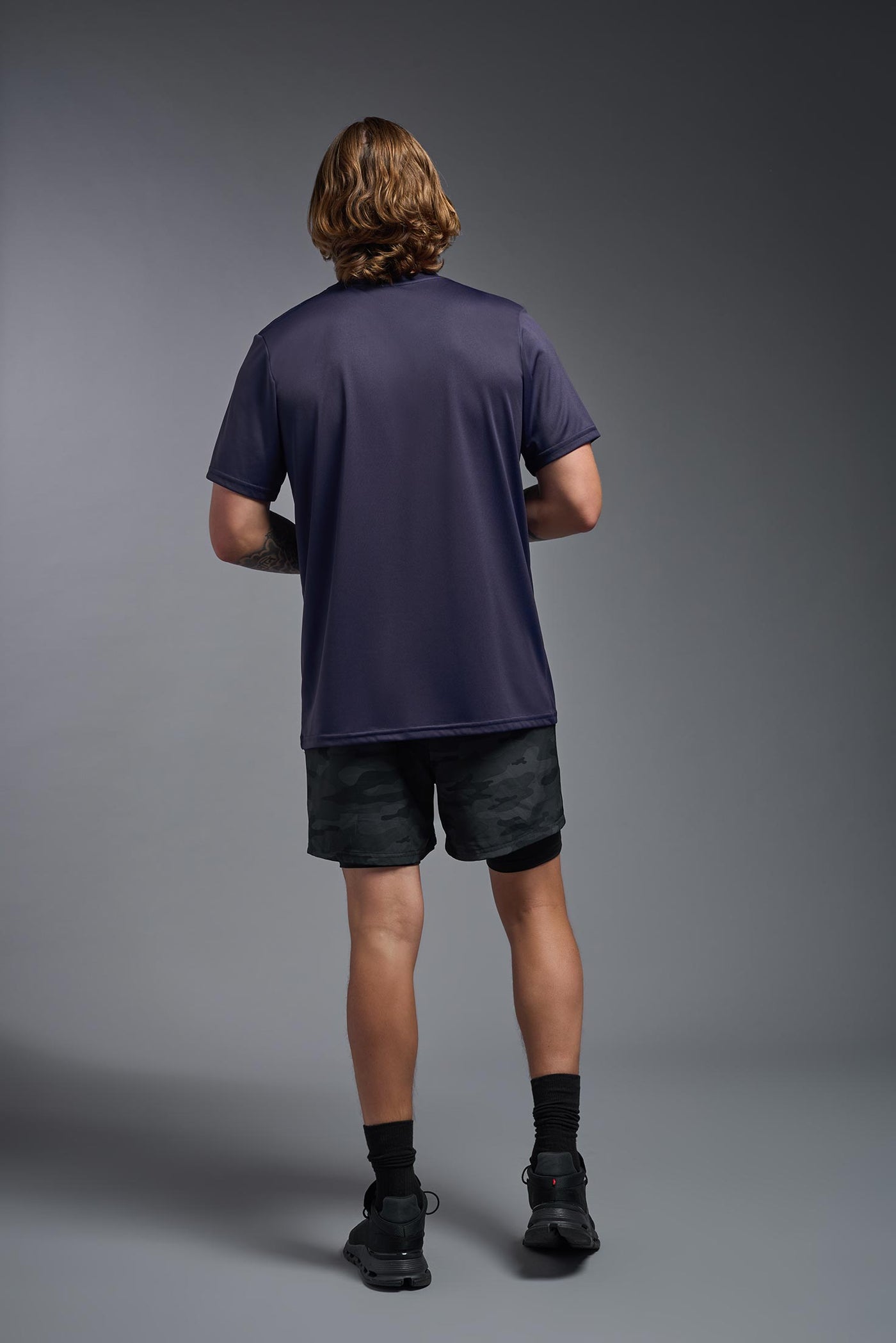 A blonde, male model with a beard wearing the men's EcoTek™ Recycled Performance Tee in the color twilight, made out of 100% recycled polyester REPREVE®, showing the modern fit from a back view. This shirt features a mechanical stretch, quick-dries, wicks moisture and is made in the USA. #color_twilight