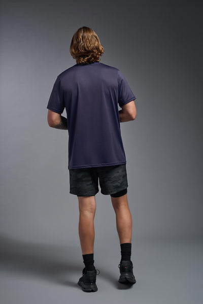 A blonde, male model with a beard wearing the men's EcoTek™ Recycled Performance Tee in the color twilight, made out of 100% recycled polyester REPREVE®, showing the modern fit from a back view. This shirt features a mechanical stretch, quick-dries, wicks moisture and is made in the USA. #color_twilight