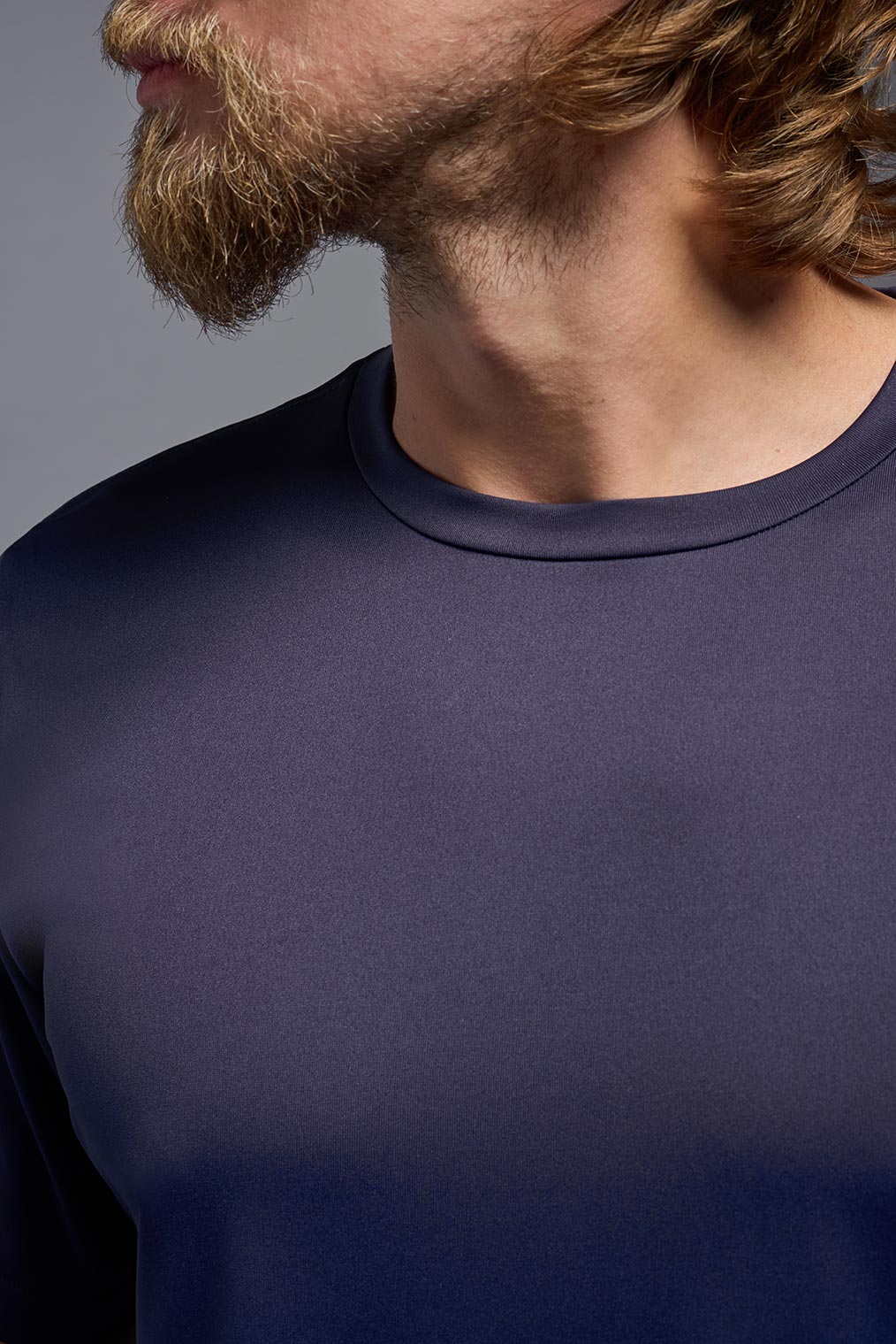 A blonde, male model with a beard wearing the men's EcoTek™ Recycled Performance Tee in the color twilight, made out of 100% recycled polyester REPREVE®, showing the modern fit from a close-up collar view. This shirt features a mechanical stretch, quick-dries, wicks moisture and is made in the USA. #color_twilight