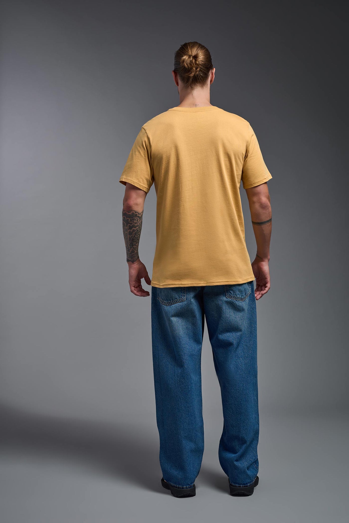 A male model wearing the unisex Organic Soft Cotton T-shirt in the color harvest, made from 100% certified organic cotton, shot from a full body back view. This shirt is unisex and made in the USA. #color_harvest