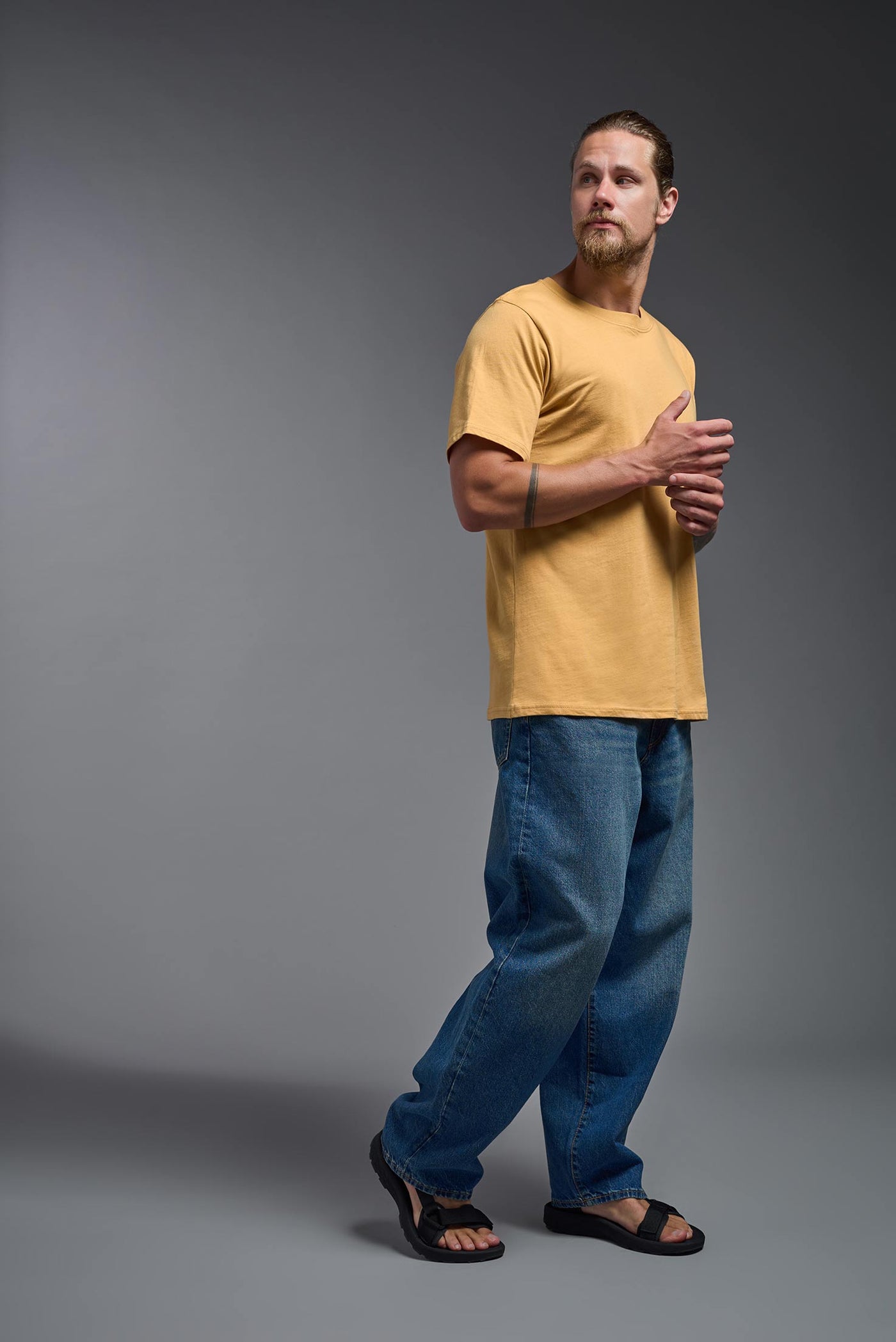 A male model wearing the unisex Organic Soft Cotton T-shirt in the color harvest, made from 100% certified organic cotton, shot from a full body side view. This shirt is unisex and made in the USA. #color_harvest
