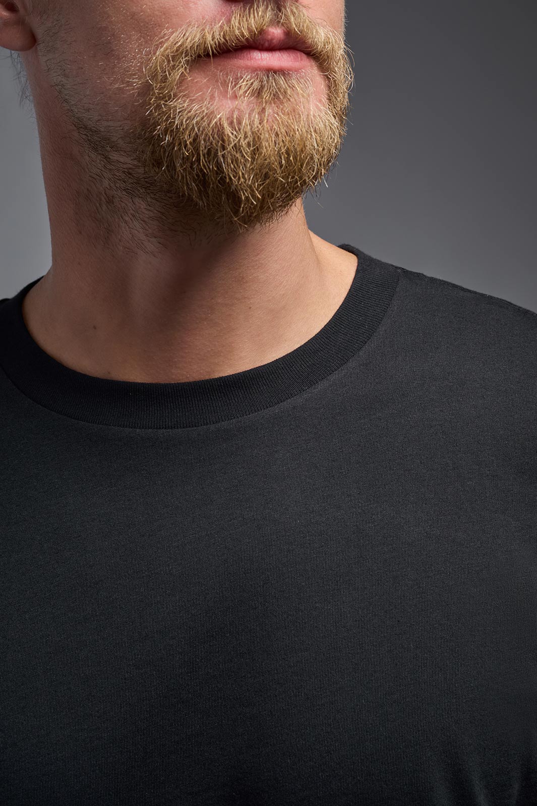 A male model wearing the unisex Organic Soft Cotton T-shirt in the color black, made from 100% certified organic cotton, shot from a closeup collar front view. This shirt is unisex and made in the USA. #color_black