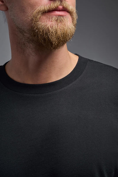 A male model wearing the unisex Organic Soft Cotton T-shirt in the color black, made from 100% certified organic cotton, shot from a closeup collar front view. This shirt is unisex and made in the USA. #color_black