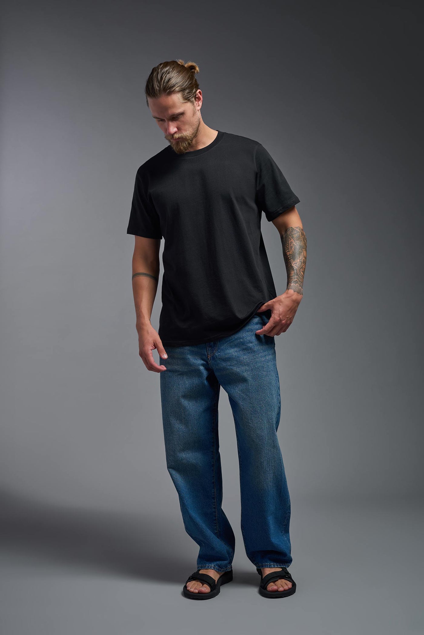 A male model wearing the unisex Organic Soft Cotton T-shirt in the color black, made from 100% certified organic cotton, shot from a full body front view. This shirt is unisex and made in the USA. #color_black