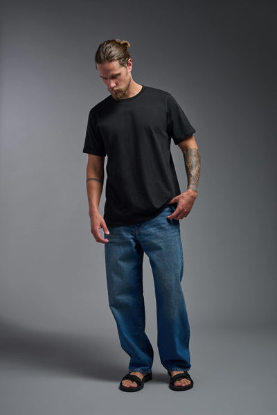 A male model wearing the unisex Organic Soft Cotton T-shirt in the color black, made from 100% certified organic cotton, shot from a full body front view. This shirt is unisex and made in the USA. #color_black