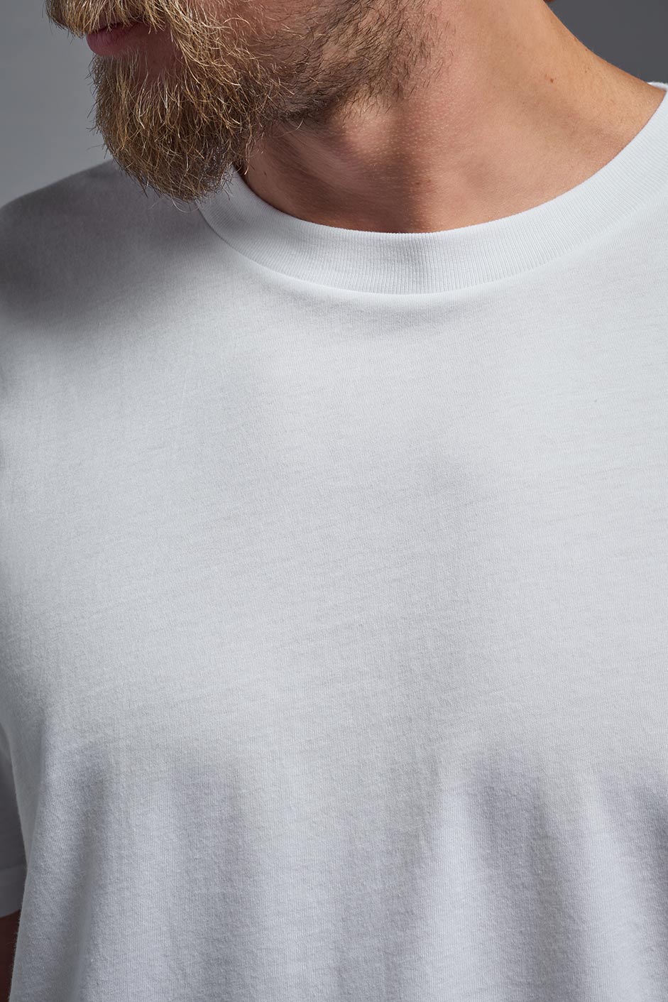 A male model wearing the unisex Organic Soft Cotton T-shirt in the color white, made from 100% certified organic cotton, shot from a closeup collar front view. This shirt is unisex and made in the USA. #color_white