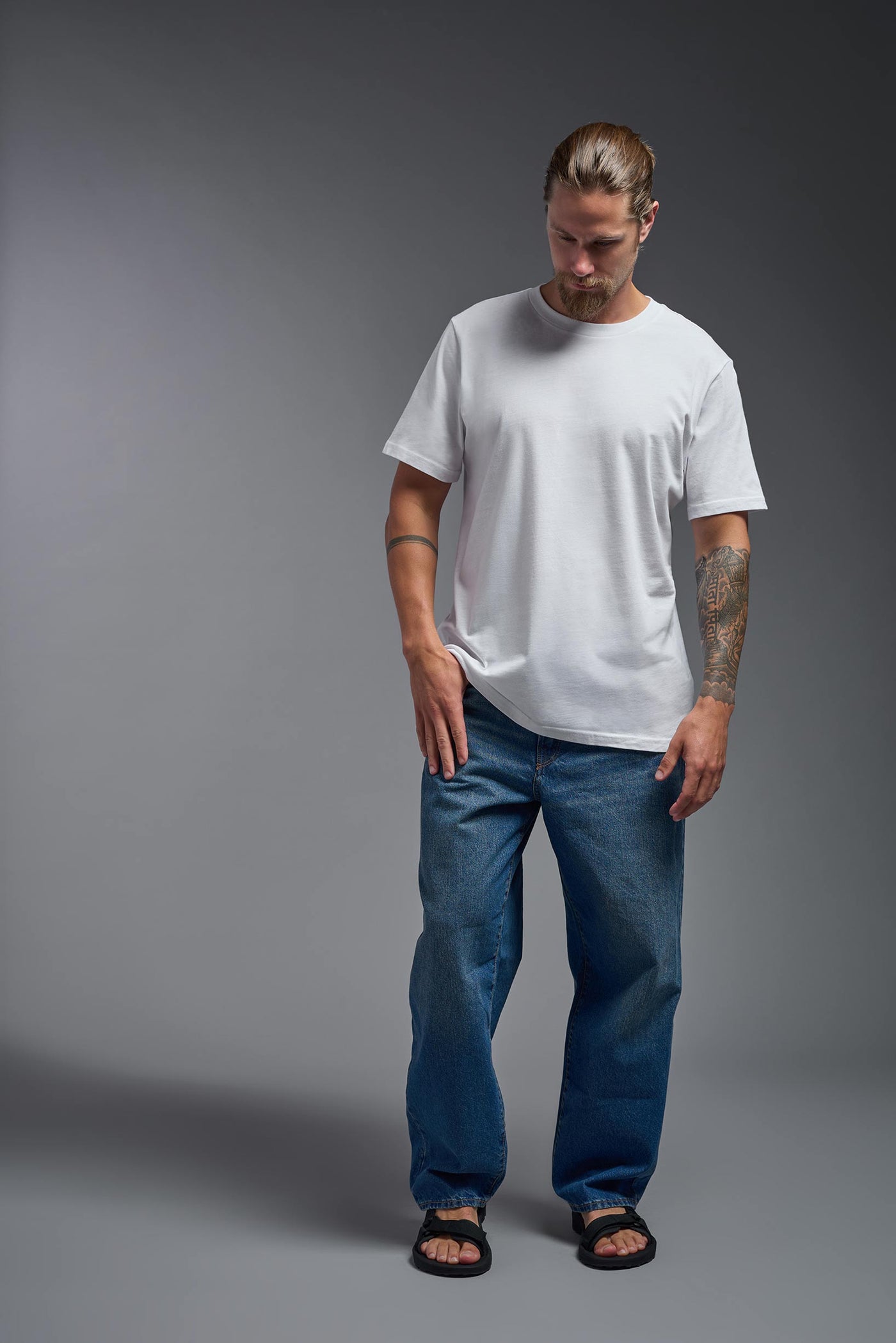 A male model wearing the unisex Organic Soft Cotton T-shirt in the color white, made from 100% certified organic cotton, shot from a full body front view. This shirt is unisex and made in the USA. #color_white