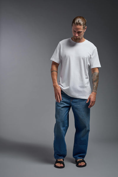 A male model wearing the unisex Organic Soft Cotton T-shirt in the color white, made from 100% certified organic cotton, shot from a full body front view. This shirt is unisex and made in the USA. #color_white