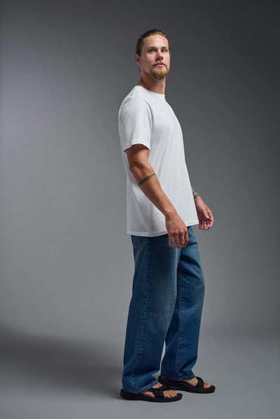 A male model wearing the unisex Organic Soft Cotton T-shirt in the color white, made from 100% certified organic cotton, shot from a full body side view. This shirt is unisex and made in the USA. #color_white