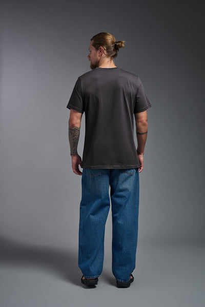 A male model wearing the unisex Organic Soft Cotton T-shirt in the color nova, made from 100% certified organic cotton, shot from a full body back view. This shirt is unisex and made in the USA. #color_carbon