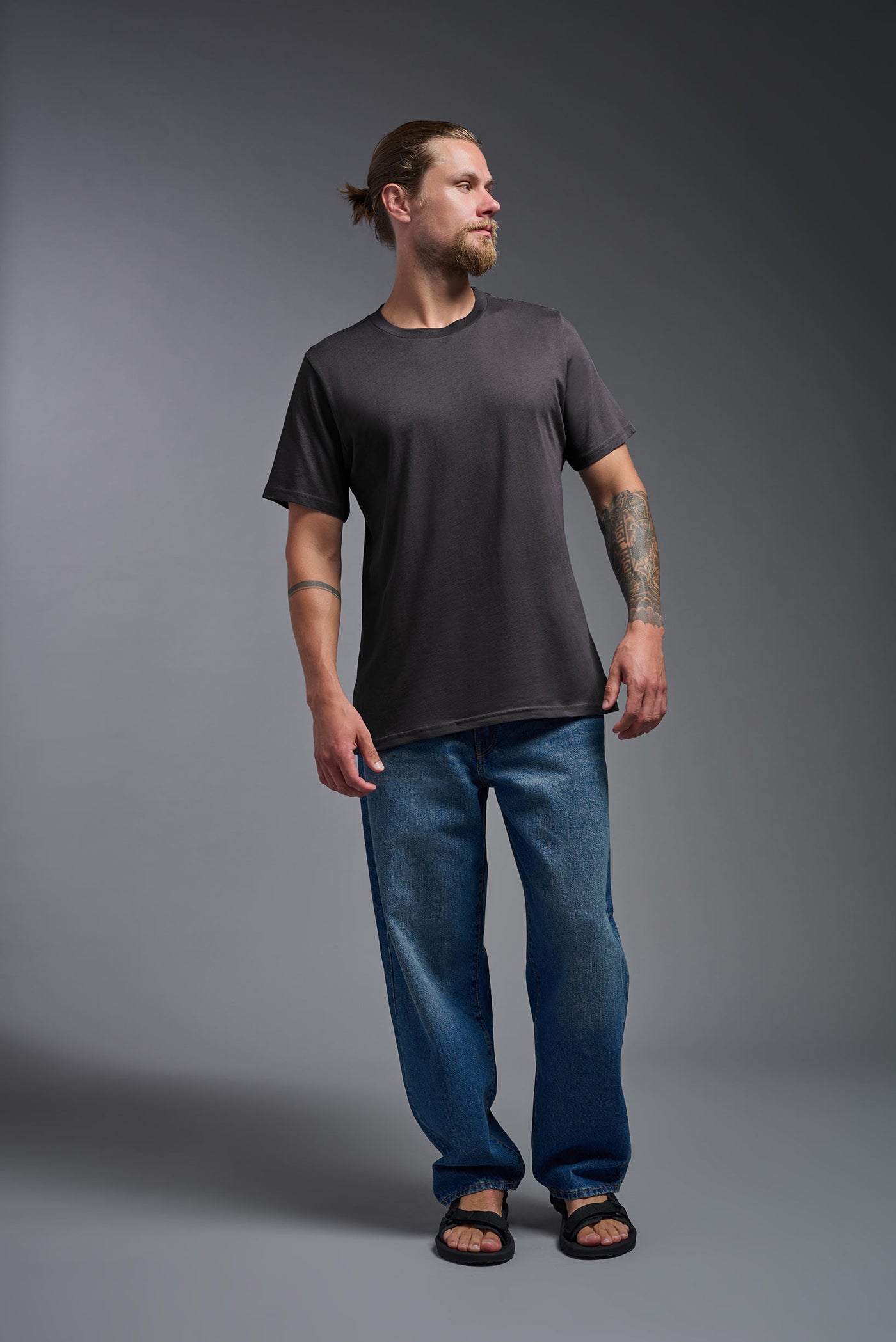 A male model wearing the unisex Organic Soft Cotton T-shirt in the color nova, made from 100% certified organic cotton, shot from a full body front view. This shirt is unisex and made in the USA. #color_carbon