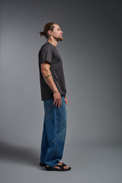 A male model wearing the unisex Organic Soft Cotton T-shirt in the color nova, made from 100% certified organic cotton, shot from a full body side view. This shirt is unisex and made in the USA. #color_carbon