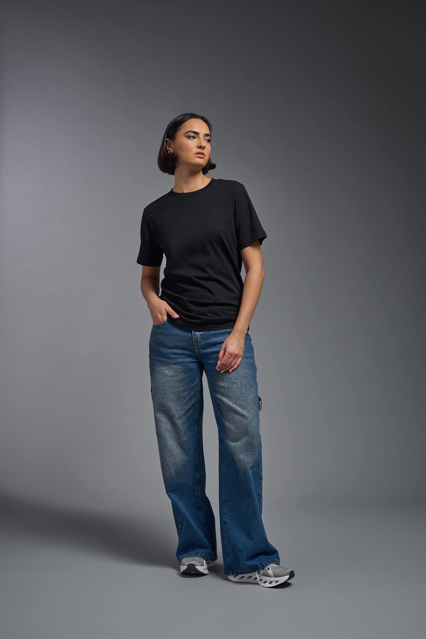 A female model wearing the unisex Organic Soft Cotton T-shirt in the color black, made from 100% certified organic cotton, shot from a full body front view. This shirt is unisex and made in the USA. #color_black