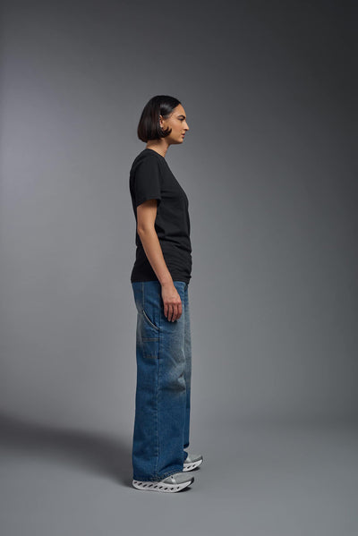 A female model wearing the unisex Organic Soft Cotton T-shirt in the color black, made from 100% certified organic cotton, shot from a full body side view. This shirt is unisex and made in the USA. #color_black