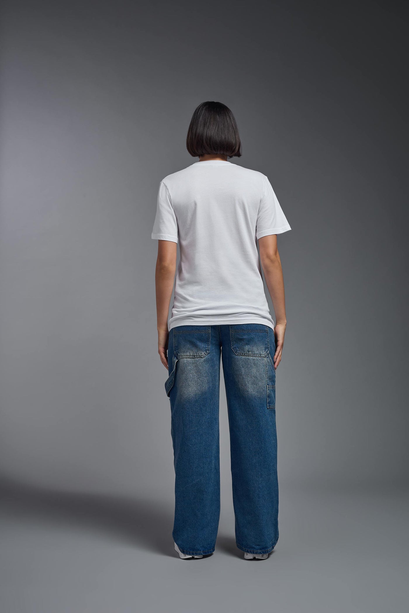 A female model wearing the unisex Organic Soft Cotton T-shirt in the color white, made from 100% certified organic cotton, shot from a full body back view. This shirt is unisex and made in the USA. #color_white
