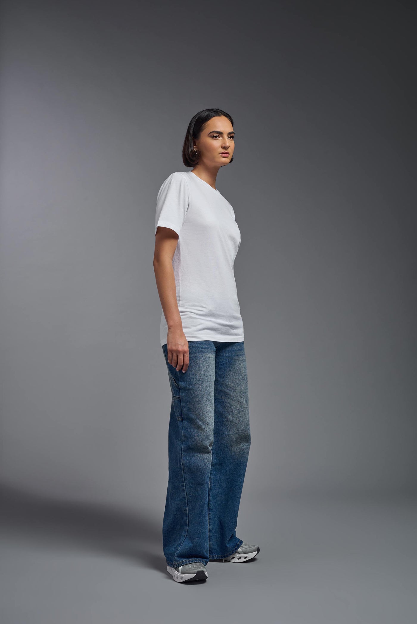 A female model wearing the unisex Organic Soft Cotton T-shirt in the color white, made from 100% certified organic cotton, shot from a full body side view. This shirt is unisex and made in the USA. #color_white