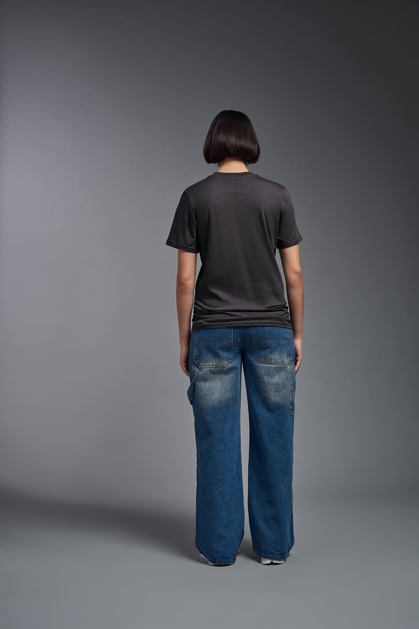 A female model wearing the unisex Organic Soft Cotton T-shirt in the color nova, made from 100% certified organic cotton, shot from a full body back view. This shirt is unisex and made in the USA. #color_carbon