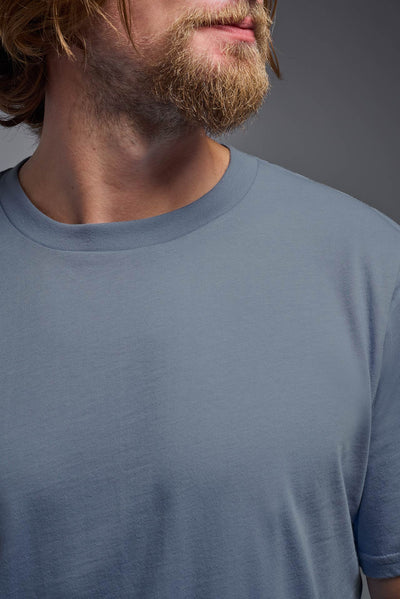 A male model wearing the unisex Organic Soft Cotton T-shirt in the color canyon blue, made from 100% certified organic cotton, shot from a closeup collar front view. This shirt is unisex and made in the USA. #color_canyon-blue